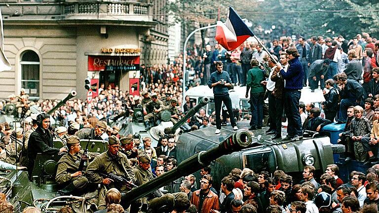 Prager Frühling       -  Im August 1968 umringen Demonstranten in der Innenstadt von Prag sowjetische Panzer und stehen mit einer Fahne der Tschechoslowakei auf einem umgekippten Militärfahrzeug. Reformpolitiker unter der Führung Alexander Dubèeks hatten vor 50 Jahren versucht, in der Tschechoslowakei einen &bdquo;Sozialismus mit menschlichem Antlitz&ldquo; zu schaffen. In der Nacht zum 21. August 1968 marschierten Truppen des Warschauer Pakts unter Führung der UdSSR in der Tschechoslowakei ein und beendeten den &bdquo;Prager Frühling&ldquo; mit Waffengewalt. Foto Libor Hajsky CTK via epa, dpa