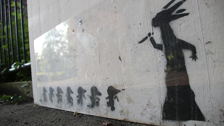 Das Graffito Horrorwittchen von Valentin Lude in der Unterführung zwischen Hauptfriedhof und Wombach, mit einer Plastiktafel geschützt.
