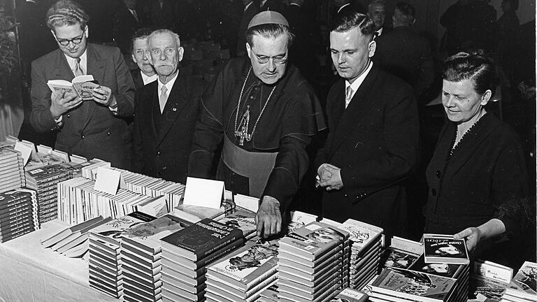 Einige Exemplare aus der reichen Auswahl der verlegten Werke seines Hauses zeigt Verleger Popp Bischof Julius Döpfner im Oktober 1955. Vor dem Büchertisch stehen Bischof Julius Döpfner, Verleger Popp und dessen Mutter. Einige Exemplare aus der reichen Auswahl der verlegten Werke seines Hauses zeigt Verleger Popp Bischof Julius Döpfner im Oktober 1955. Vor dem Büchertisch stehen Bischof Julius Döpfner, Verleger Popp und dessen Mutter. 
