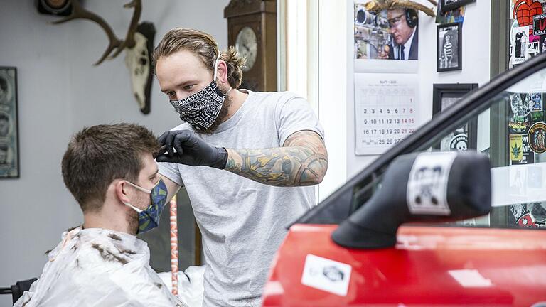 Sicheres Arbeiten dank Schrottteilen: Eine Autotüre trennt die Arbeitsplätze der Friseure des 'Booder' in Haßfurt. Marco Maas (rechts) hat den ersten Arbeitstag unter erschwerten Bedingungen hinter sich gebracht.