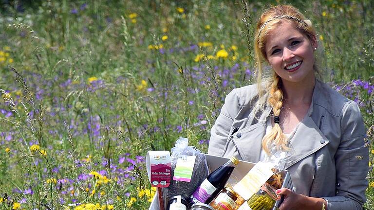 Lisa Majewski präsentiert die Rhönwiese-Geschenkbox inmitten einer typisch blühenden Rhönwiese.