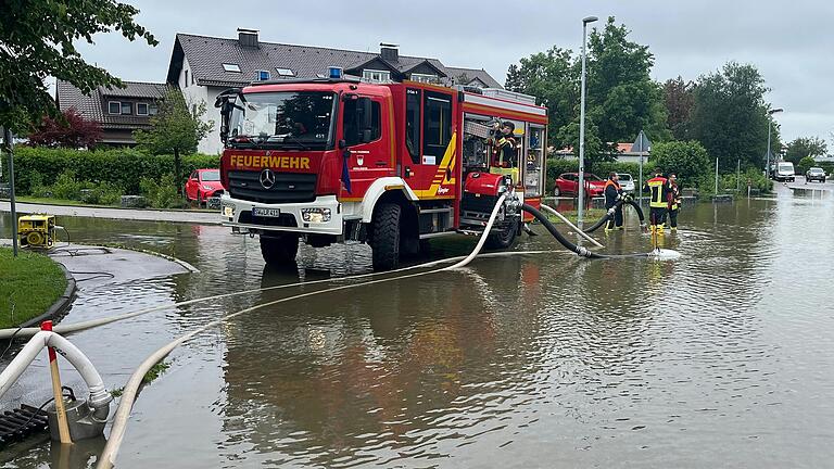 Einsatzkräfte der Feuerwehr Gerolzhofen pumpen am Sonntagvormittag Wasser von einer überfluteten Straßenkreuzung in Mering im Landkreis Aichach-Friedberg.