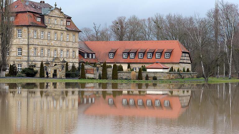 Die ehemalige 'Seniorenresidenz Schloss Gleusdorf' spiegelt sich in einer überfluteten Wiese. Die Einrichtung soll nach Übernahme durch die MCC-Gruppe als „MCC Haus im Park“ in Untermerzbach optimistisch in die Zukunft blicken.