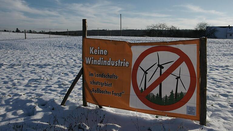 Die Gegner eines Windparks im Roßbacher Forst machen erneut mobil, hier mit einem Aufsteller am Ortsrand von Roßbach, im Hintergrund das mutmaßlich betroffene riesige Waldstück.       -  Die Gegner eines Windparks im Roßbacher Forst machen erneut mobil, hier mit einem Aufsteller am Ortsrand von Roßbach, im Hintergrund das mutmaßlich betroffene riesige Waldstück.