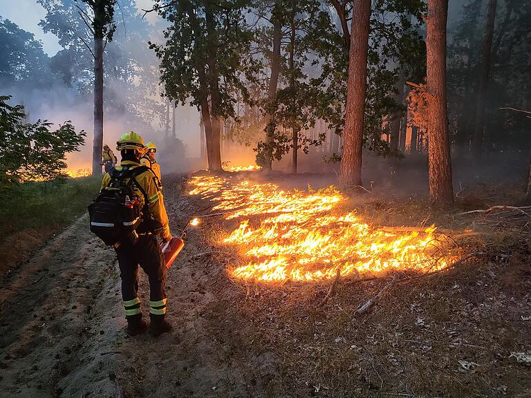 Ein Feuerwehrmann legt mit einer Ölkanne das Vorfeuer aus. Eine in Deutschland sehr seltene Methode, die viel Erfahrung braucht.