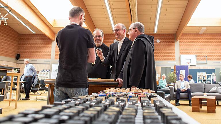 Auch Bischof Franz Jung besuchte die Büchertage und nahm sich in Begleitung von Abt Michael Reepen OSB und Verlagsleiter Bruder Ansgar Stüfe Zeit an den einzelnen Ständen. Hier wird ihm am Stand der Klostermanufaktur die neue Designlinie 'Zusammengewürfelt' gezeigt, die ihn faszinierte. Aus Metallwerkstatt, Goldschmiede, Schreinerei und Kunstatelier werden Unikate in Würfelform gefertigt, die symbolisch für die zusammengewürfelte Klostergemeinschaft stehen und in ihrem Design Geschichten erzählen. Auch Bischof Franz Jung besuchte die Büchertage und nahm sich in Begleitung von Abt Michael Reepen OSB und Verlagsleiter Bruder Ansgar Stüfe Zeit an den einzelnen Ständen. Hier wird ihm am Stand der Klostermanufaktur die neue Designlinie 'Zusammengewürfelt' gezeigt, die ihn faszinierte. Aus Metallwerkstatt, Goldschmiede, Schreinerei und Kunstatelier werden Unikate in Würfelform gefertigt, die symbolisch für die zusammengewürfelte Klostergemeinschaft stehen und in ihrem Design Geschichten erzählen.