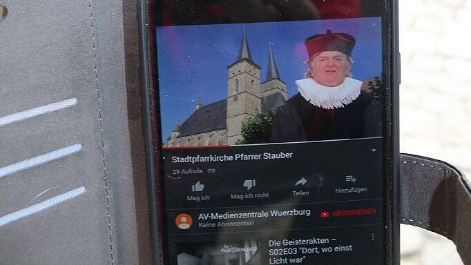 Wenn man auf seiner Geo-Caching-Tour durch die Gerolzhöfer Altstadt die versteckten Aufkleber mit den QR-Codes entdeckt und die Codes mit einer App eingelesen hat, dann öffnen sich auf dem Handy kleine Videos, in denen Schauspieler des Wandeltheaters Tipps für die nächste Station geben und jeweils ein Rätsel für einen Zahlencode stellen. Bei einer der Stationen ist Bernd Beck als &bdquo;Pfarrer Stauber&ldquo; zu sehen.