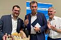 Demonstrativ biss Bayerns Ministerpräsident Markus Söder beim Bezirksparteitag in Niedernberg in die Wurst aus dem Präsentkorb, den ihm der Miltenberger Kreisvorsitzende Michael Schwing (links) überreicht hatte. Der wiedergewählte Bezirksvorsitzende Steffen Vogel (rechts) applaudierte.