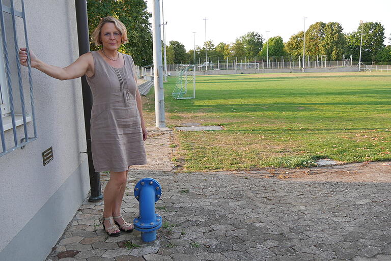 Sitta Kaufmann, die Vorsitzende des Sportvereins Bergtheim verweist an der Entnahmestelle der Zisterne auf das kleine neue Schild an der Hauswand. 'Kein Trinkwasser' steht dort. Im Hintergrund ist der Trainingsplatz des SVB zu sehen. Er wird mit dem Wasser aus der Zisterne und damit mit Grund- und Niederschlagswasser bewässert. Sitta Kaufmann, die Vorsitzende des Sportvereins Bergtheim verweist an der Entnahmestelle der Zisterne auf das kleine neue Schild an der Hauswand. 'Kein Trinkwasser' steht dort. Im Hintergrund ist der Trainingsplatz des SVB zu sehen. Er wird mit dem Wasser aus der Zisterne und damit mit Grund- und Niederschlagswasser bewässert.