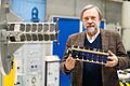 Der Wissenschaftler und Präsident des Zentrums für Telematik, Klaus Schilling, steht vor einem Dynamiksimulator, an dem ein NetSat-Pico-Satellit angebracht ist und hält ein Modell eines solches Kleinstsatelliten in den Händen. Würzburger Wissenschaftler wollen den Weg bereiten, um von 2022 an mithilfe von Verfahren ähnlich der Computertomographie ins Innere von Wolken zu blicken.