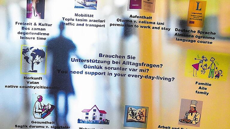 Migrationsberatung       -  Blick durch eine Folie mit Hinweisen zur Unterstützung bei Alltagsfragen in unterschiedlichen Sprachen. Menschen, die sich hier eine neue Zukunft aufbauen wollen, haben zahlreiche Hürden zu nehmen, um Fuß zu fassen.
