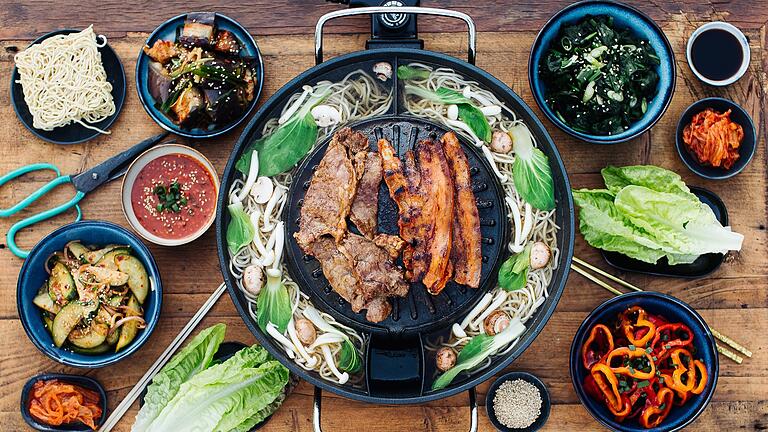 Koreanische Küche - Hotpot       -  Koreanisches BBQ ist die beliebte Methode, Fleisch direkt am Esstisch zuzubereiten. Mariniertes Fleisch wird gegrillt, anschließend in ein Salatblatt gewickelt und in eine scharfe Sauce getunkt. Das genießt man zusammen mit verschiedenen Beilagen und Sauce zum Dippen.