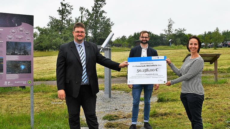 Ulrike Schade übergab den symbolischen Scheck an Bürgermeister Christoph Friedrich. Schade und die Mitarbeiterinnen und Mitarbeiter aus der Thüringer Verwaltung des Biosphärenreservats (hier  Frank Riedel, Mitte) begleiten die Kommunen bei der Umsetzung der Projekte im Rahmen des Förderprogramms. Auf der Fläche im Hintergrund wird der Sky-Pole errichtet.  Foto: Anna-Lena Bieneck       -  Ulrike Schade übergab den symbolischen Scheck an Bürgermeister Christoph Friedrich. Schade und die Mitarbeiterinnen und Mitarbeiter aus der Thüringer Verwaltung des Biosphärenreservats (hier  Frank Riedel, Mitte) begleiten die Kommunen bei der Umsetzung der Projekte im Rahmen des Förderprogramms. Auf der Fläche im Hintergrund wird der Sky-Pole errichtet.  Foto: Anna-Lena Bieneck