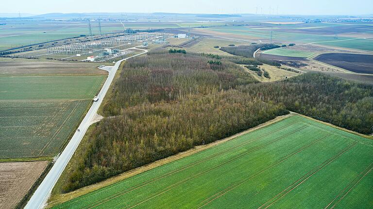 Genau zwischen Umspannwerk West (im Bild oben links) und dem künftigen Konverter auf dem etwa 500 Meter entfernten Acker&nbsp; (im Bild vorne rechts) liegt der Bergrheinfelder Klimawald. Mitten hindurch möchte Tennet den im Konverter ankommenden SuedLink zum Umspannwerk führen. Dazu müsste eine Schneise in den Wald geschlagen werden. Alternativ könnte die Freileitung über den Wald oder um den Wald herumgeführt werden.