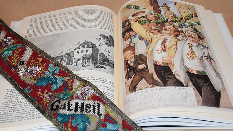 Schon der Ausschnitt des Turnergürtels zeigt, wie viel Arbeit in dieser Stickerei steckt. In dem Buch mit historischen Abbildungen sind junge Männer zu sehen, die mit Turnergürteln geschmückt zu einem Turnerfest in Nürnberg kommen.