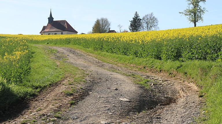 Der ausgeschwemmte Flurweg am Brachberg mit Blick auf die Sulzthaler Kreuzkapelle. Der Einbau der „Homburger Kante“ soll hier Abhilfe schaffen.       -  Der ausgeschwemmte Flurweg am Brachberg mit Blick auf die Sulzthaler Kreuzkapelle. Der Einbau der „Homburger Kante“ soll hier Abhilfe schaffen.