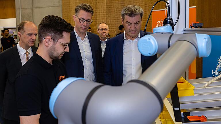 Doktorand Philipp Kranz erklärt (von rechts) Ministerpräsident Markus Söder, Wissenschaftsminister Markus Blume und THWS-Präsident Robert Grebner einen Roboter, der bei Montagearbeiten unterstützt. Im Hintergrund CERI-Leiter Tobias Kaupp.