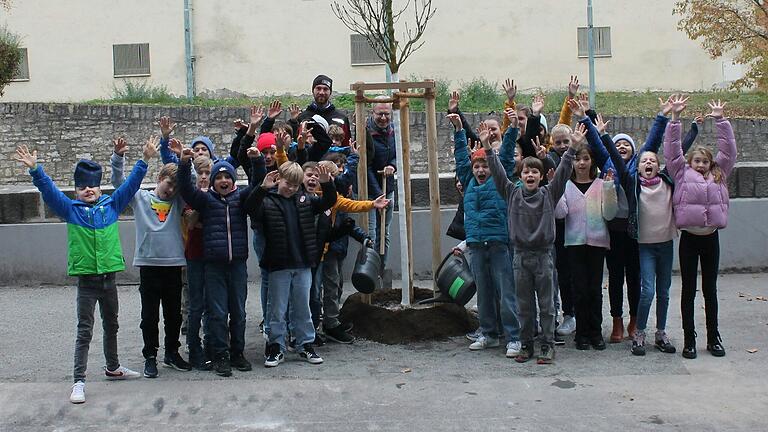 Schülerinnen und Schüler des DHG bejubeln den neu gepflanzten Baum, dahinter in der Bildmitte mit Spaten: Schulleiter Michael Schmitt und die Mitarbeiter der Gartenbaufirma Lindner.