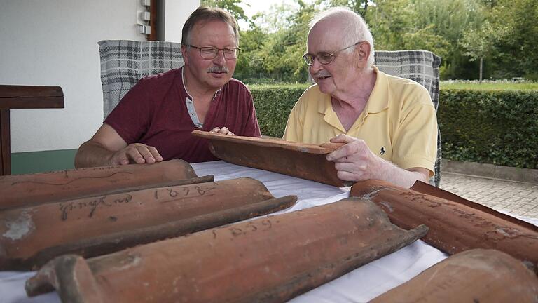 Rainer Elflein (links) hat vor Kurzem mehrere historische Dachziegel vom Dachboden seines Elternhauses in Lendershausen geholt. Rudolf Ludwig schaffte es, Teile der Inschriften zu entziffern.