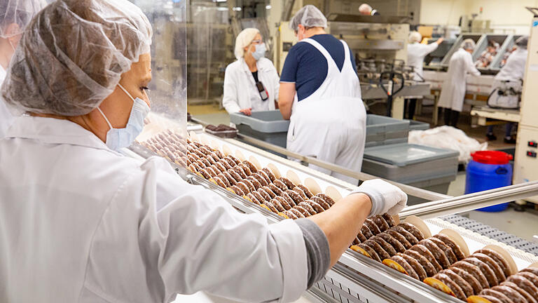 Lebkuchen Schmidt in Nürnberg: Auch wenn die Halle voller Maschinen steht – in der  Lebkuchenfabrik geht nichts ohne Menschen. Mitarbeiterinnen und Mitarbeiter haben die Produktion unter Kontrolle – und füllen Schachteln.