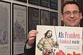 Museumsleiter Markus Mergenthaler präsentiert im Gang mit der Plakatgalerie das aktuelle Plakat zur Ausstellung.