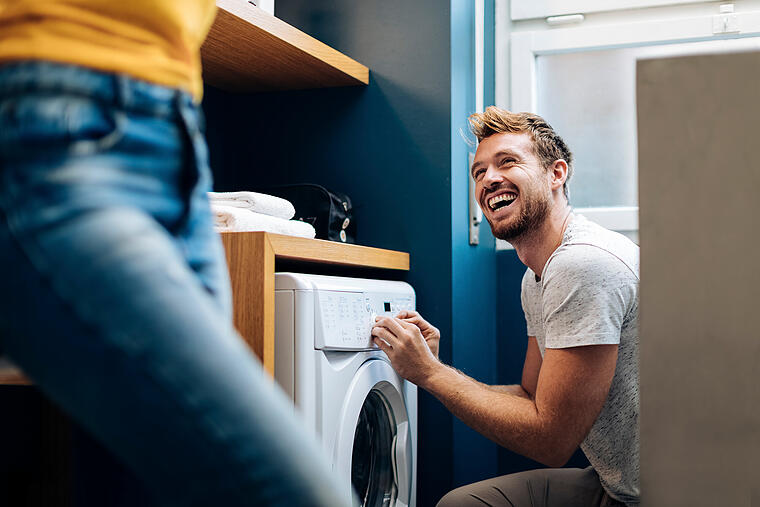 Happy young man looking at girlfriend and doing the laundry at home       -  Mit der WVV EnergieSparPrämie 60 € Zuschuss sichern.