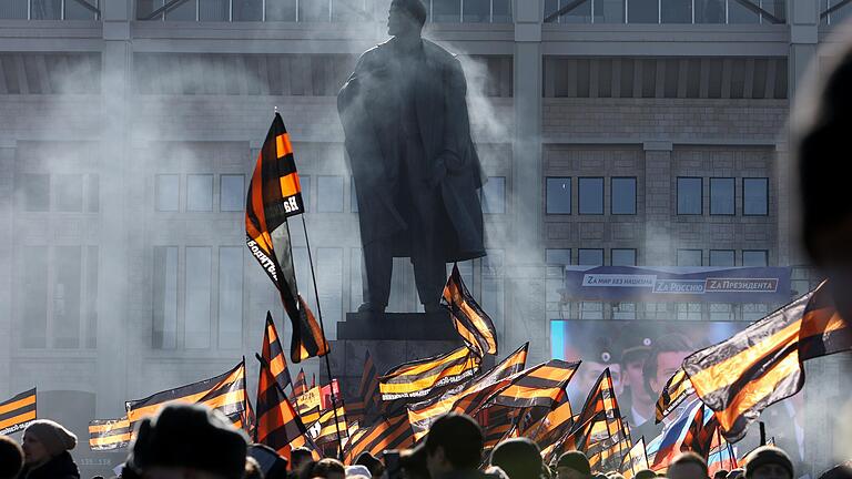 Menschen in Moskau halten Fahnen in den Farben des Sankt-Georgs-Bands, ein russisches militärisches Abzeichen, um ihre Unterstützung für Präsident Putin auszudrücken. Im Hintergrund ein Lenin-Denkmal.