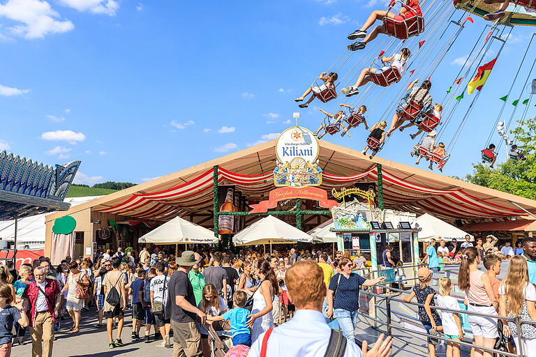 Das Kiliani-Festzelt bei strahlendem Sonnenschein am Familiennachmittag: Scheinbar schwerelos fliegt das Kettenkarussell über die Besucher.