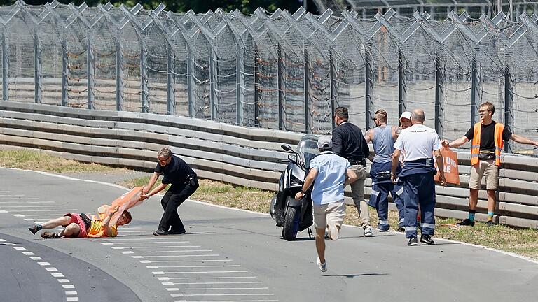 Verursachten eine 15-minütige Verzögerung beim Start des Norisring-Rennens am Sonntag: Streckenposten zerren einen Protestler der 'Letzten Generation' von der Rennstrecke, während ein zweiter am Zaun klebt. Verursachten eine 15-minütige Verzögerung beim Start des Norisring-Rennens am Sonntag: Streckenposten zerren einen Protestler der 'Letzten Generation' von der Rennstrecke, während ein zweiter am Zaun klebt.