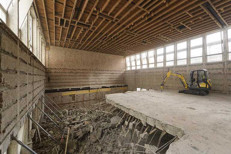 Der Minbagger mit Abbruchmeißel zerlegt den Betonboden der Turnhalle. Der Minbagger mit Abbruchmeißel zerlegt den Betonboden der Turnhalle. 