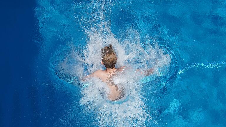 Schwimmbad       -  Ein Junge springt in einem Freibad ins Wasser.