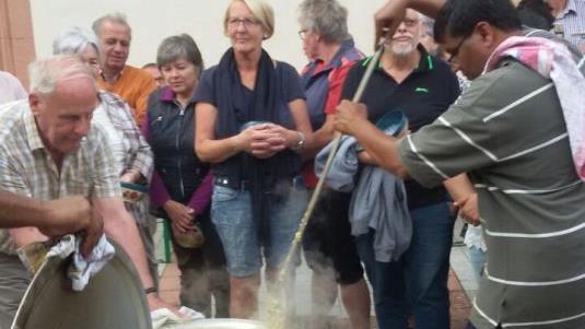 Pater Raja schwingt den großen Kochlöffel am Aschacher Dorfplatz. Er kochte in einem eigens aus Indien mitgebrachten Topf ein Gericht.  Foto: Sigrid Klemke       -  Pater Raja schwingt den großen Kochlöffel am Aschacher Dorfplatz. Er kochte in einem eigens aus Indien mitgebrachten Topf ein Gericht.  Foto: Sigrid Klemke