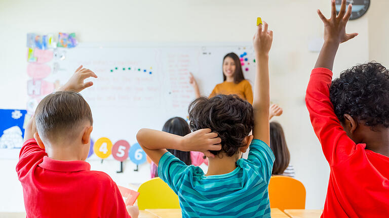 Preschool kid raise arm up to answer teacher question on whiteboard in classroom,Kindergarten education concept       -  Symbolbild: Schule