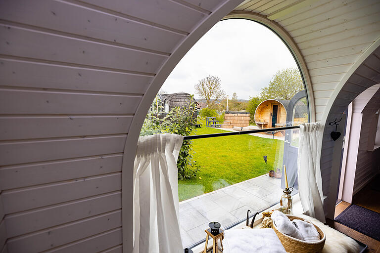 Ausblick aus einem der Tiny Houses über den grünen Rasen auf die Fass-Sauna und den links daneben gelegenen Hot Tub.