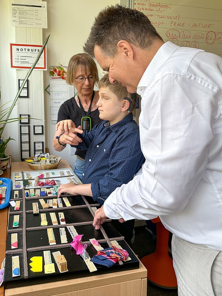 Jürgen Dusel lässt sich von Lucas und seiner Lehrerin Maria-Rascher-Wolfring den taktilen Stundenplan des taubblinden Schülers erklären. Jürgen Dusel lässt sich von Lucas und seiner Lehrerin Maria-Rascher-Wolfring den taktilen Stundenplan des taubblinden Schülers erklären. 