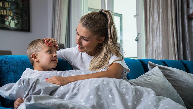 Eine Mutter fasst ihrem Sohn prüfend an die Stirn       -  Muss das Fieber des Kindes runter, dann helfen Wirkstoffe Paracetamol und Ibuprofen. ASS hingegen ist für Kinder unter 12 Jahren tabu.