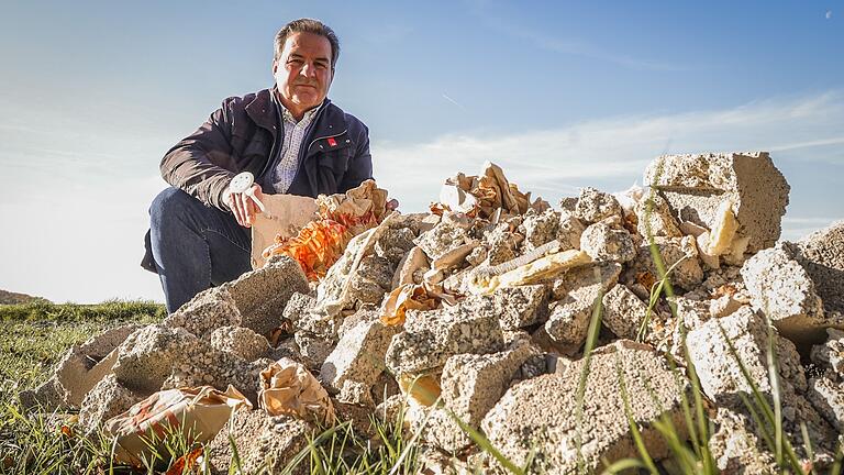 Aidhausens Bürgermeister Dieter Möhring sitzt neben einem kleinen Berg aus Bauschutt, den Unbekannte am Nassacher See entsorgt haben.&nbsp;