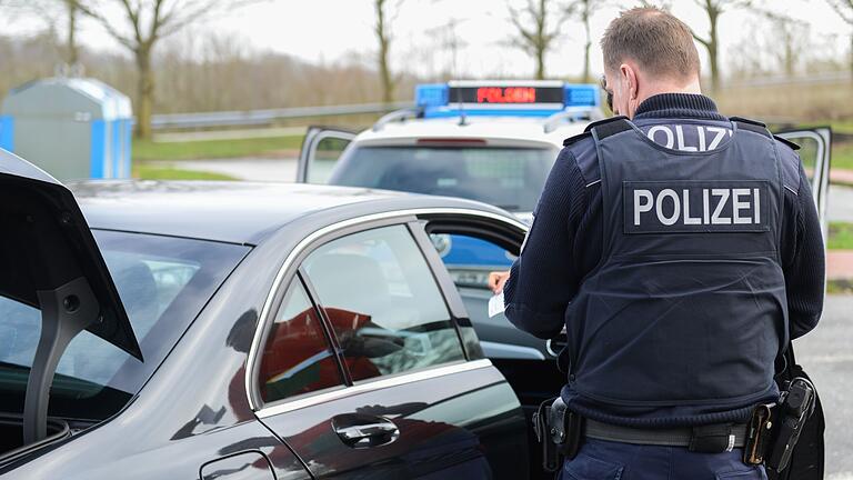 Ein Polizeibeamter überprüft bei einer  Verkehrskontrolle einen Autofahrer und dessen Fahrzeug.&nbsp;