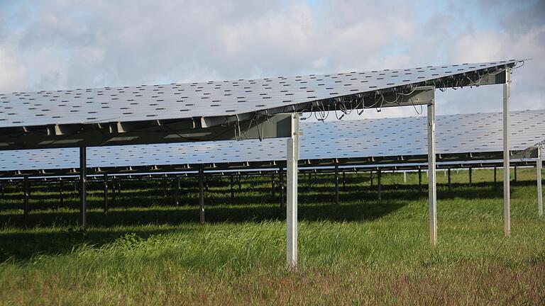 Die je nach Sonnenintensität stark schwankende Ausbeute von Photovoltaikanlagen, wie von dieser Freiflächenanlage bei Alitzheim (Lkr. Schweinfurt), erschwert nach Aussagen der ÜZ Mainfranken Stromversorgern die Kalkulation der einzukaufenden Strommengen und treibt den Strompreis für Kunden über verteuerte Netzentgelte zusätzlich in die Höhe.