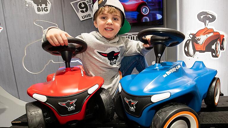 Neuheitenschau der Spielwarenmesse - Ein Junge sitzt während der Neuheitenschau der Spielwarenmesse zwischen zwei Big-Bobby-Cars. Neuheitenschau der Spielwarenmesse - Ein Junge sitzt während der Neuheitenschau der Spielwarenmesse zwischen zwei Big-Bobby-Cars.
