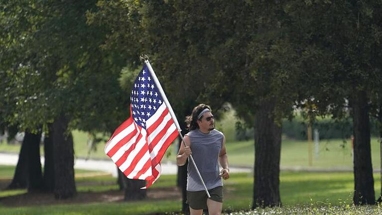 Ein Mann joggt mit einer Nationalflagge der Vereinigten Staaten eine Straße in Houston (Texas) entlang. Am 4. Juli feiern US-Amerikaner jedes Jahr ihren Unabhängigkeitstag. Foto: David J. Phillip/AP/dpa       -  Ein Mann joggt mit einer Nationalflagge der Vereinigten Staaten eine Straße in Houston (Texas) entlang. Am 4. Juli feiern US-Amerikaner jedes Jahr ihren Unabhängigkeitstag.