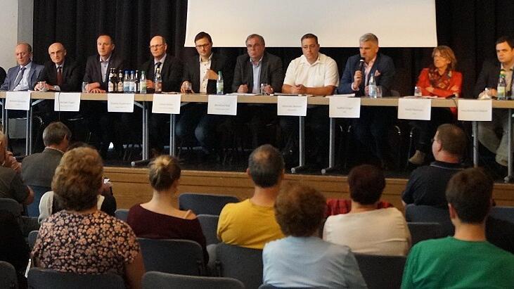 Der &bdquo;Runde Tisch&ldquo; war hätte wohl eher &bdquo;langer Tisch&ldquo; heißen müssen. Auf dem Podium saßen (von links) Petra Hohenberger vom Hallenbadverein, Susanne Makowski vom BLSV, Horst Hofmann vom Zweckverband Schule, Landrat Wilhelm Schneider, der Eltmanner Bürgermeister Michael Ziegler, der Zeiler Bürgermeister Thomas Stadelmann, BI-Sprecher Julian Müller, der Sander Bürgermeister Bernhard Ruß, Johannes Rennert von der Wasserwacht, die Landtagsabgeordneten Steffen Vogel und Kathi Petersen, Dorothee Bärs Büroleiter Paul-Bernhard Wagner und Moderator Fabian Weber.