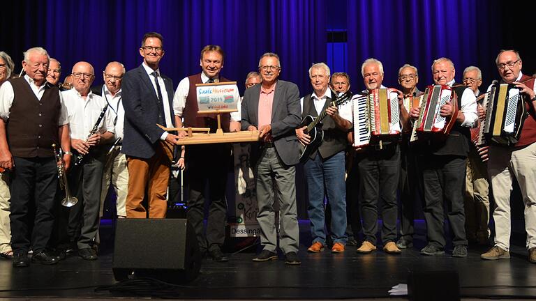 Bei der Zentralveranstaltung des Saale-Musicums in der Stadthalle wurde das symbolische Floß aus dem Kreis Rhön-Grabfeld an den Kreis Bad Kissingen weitergereicht. Die stellvertretenden Landräte Peter Suckfüll (Rhön-Grabfeld) und Emil Müller (Bad Kissingen) fanden sich zur Übergabe mit Saale-Musicum-Initiator Kuno Holzheimer unter der Aufsicht der Prominentenband Bad Königshofen ein.