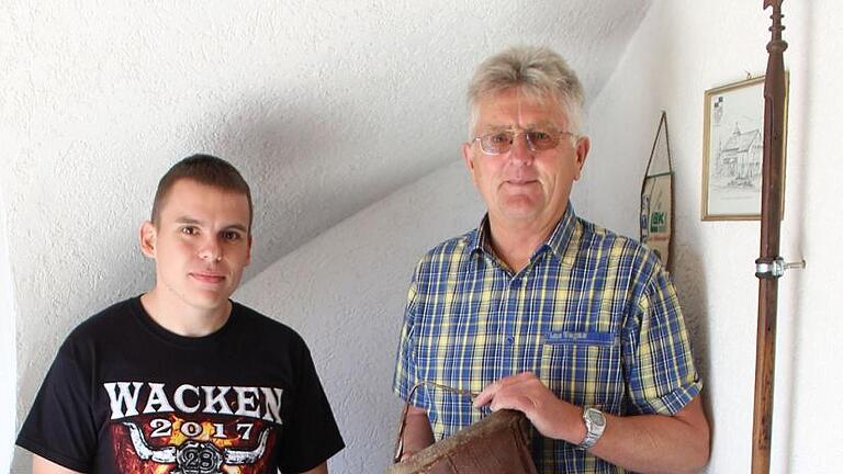 Feuerwehr-Vorsitzender Benjamin Diaz Sanchez (links) und Fred Bock, seit 1969 Aktiver in den Reihen der Wehr und seit 1998 Schriftführer, präsentieren historische Stücke der Feuerwehr, so die Motorspritze Baujahr 1934 und den jahrhundertealten Löscheimer. Rechts im Bild: die von Haus zu Haus weitergegebene Lanze der früheren Kirchenwache, die zu Gottesdienstzeiten ihre Runde im Dorf drehte.