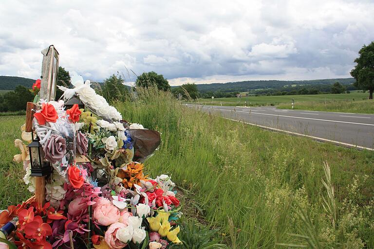 Unweit der Kreuzung erinnert am Straßenrand ein blumengeschmücktes Holzkreuz an den an dieser Stelle am 21. Mai 2023 bei einem Verkehrsunfall tödlich verunglückten 23-jährigen Familienvater.