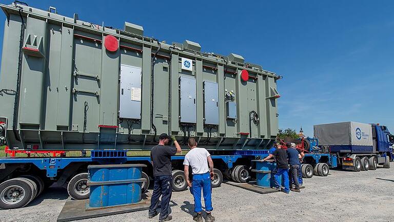 Schwertransport der besonderen Art - Dienstagmorgen an der Garstadter Schleuse, die Kiebitze haben es sich schon bequem gemacht. Auf dem Faltstuhl direkt am Ufer, bester Blick auf den Main. Kaum angekommen, geht's auch schon los: Aus Wipfeld schippert ein Schubverband Richtung Unterwasser der Garstadter Schleuse. Seine Ladung: ein mächtiger 261 Tonnen schwerer Transformator, der im neuen TenneT-Umspannwerk in Bergrheinfeld eingebaut wird. Die holländische Firma Van der Wees aus Dordrecht ist auf solche Spezialtransporte auf dem Wasser spezialisiert. Von Krefeld über den Rhein und ab Wiesbaden den Main hinauf fuhr der Schubverband mit dem „Lastdrager 19“ voraus gut eine Woche lang, um seine Fracht hierher zu bringen. Ohne Probleme, wie Heiko Fröhner, stellvertretender Amtsleiter des Wasserstraßen- und Schifffahrtsamtes Schweinfurt, betont: „Auf der Wasserstraße läuft immer alles super“, sagt Fröhner lachend, „wir sind voll im Zeitplan.“ Die Arbeiter gehen routiniert ihrem Job nach, die Kiebitze am Ufer kommentieren diesen ebenso routiniert. Zunächst wurde der zwölfachsige Tieflader unter die Transportkonstruktion für den Trafo geschoben, dann der Trafo auf den Tieflader abgelassen – mit Wasserwaage und Metermaß auf den Millimeter genau eingestellt. Das ist wichtig, denn um vom 68 Meter langen und neuneinhalb Meter breiten so genannten „Drive-in Ponton“ zu kommen, muss eine rund 30 Grad steile Rampe ans Ufer überwunden werden. Mit schweren Stahlplatten, per Autokran hingezirkelt, hat die Transportfirma Daher aus Hanau den Weg bereitet, um das Ungetüm an Land zu bringen. Nach rund eineinhalb Stunden ist alles gesichert, der erste Versuch, den Trafo rauszuziehen kann starten. Doch die Zugmaschine, ein vierachsiger Mercedes Actros kann trotz V8-Diesel und stattlichen 650 Pferdestärken nichts ausrichten, die Räder drehen an der Rampe auf dem Stahl durch. Ruhe bewahren ist die oberste Devise bei Schwertransporten, die Firma Daher tut es. Zweite Zugmaschine dran, noch mal 650 PS, zweiter Versuch – wieder nichts. Gut, ist ja nicht so, dass man nicht ausgerüstet wäre. Mit der dritten Zugmaschine – alle drei Fahrzeuge sind mit Stahlstangen verbunden – und nun elf angetriebenen Achsen hat der 261-Tonnen-Trafo keine Chance mehr, er lässt sich locker aus dem Ponton ziehen. Die Fahrt nach Bergrheinfeld ins Umspannwerk ist dann Routine, auch wenn sie aufgrund einiger enger Kurven und Kreisel durchaus größere Lenkkünste vom Lastwagenfahrer benötigt. Im Umspannwerk ist der Trafo dafür da, den herbeiströmenden 380 Kilovolt-Strom auf 110 Kilovolt herunter zu regeln, um ihn in der Region zu verteilen. Im vergangenen Sommer wurde schon ein für die so genannte Blindleistung benötigter 360 Tonnen schwerer Phasenschieber eingebaut, im Februar diesen Jahres wurden drei Kompensationsspulen in Bergrheinfeld an der Mainlände ausgeladen und ins Umspannwerk gebracht. Im neuen Umspannwerk „Bergrheinfeld West“ investiert TenneT 100 Millionen Euro. Die Kompensationsspulen braucht man zur Regulierung der so genannten Blindleistung im Stromnetz, die physikalisch bedingt entsteht. Früher wurde die für den Netzbetrieb notwendige Blindleistung vom Atomkraftwerk Grafenrheinfeld geliefert, nach dessen Abschaltung übernimmt Bereitstellung und Kompensation der Blindleistung Netzbetreiber. Auch der Phasenschieber wird dafür gebraucht, währenddessen die Transformatoren dazu da sind, den Strom so zu regeln, dass er in der Region verteilt werden kann. Die auf Garstadter Gemarkung stehende Anlage ist eine der modernsten in Deutschland und das wichtigste Umspannwerk in Nordbayern. Anfang 2019 wird das neue Umspannwerk voll einsatzfähig sein. Laut TenneT wird das alte Umspannwerk Bergrheinfeld zurückgebaut, die Anlage neben dem ehemaligen Atomkraftwerk bleibt aber erhalten. Außerdem ist man noch auf Standortsuche für die nötige Konverterhalle, die für den Anschluss der Gleichstromtrasse „Südlink“ benötigt wird. ONLINE-TIPP Viele Bilder unter www.mainpost.de/schweinfurt Ein Video vom Transport vom Schiff finden Sie unter www.facebook.com/schweinfurter.tagblatt Schwertransport der besonderen Art - Dienstagmorgen an der Garstadter Schleuse, die Kiebitze haben es sich schon bequem gemacht. Auf dem Faltstuhl direkt am Ufer, bester Blick auf den Main. Kaum angekommen, geht's auch schon los: Aus Wipfeld schippert ein Schubverband Richtung Unterwasser der Garstadter Schleuse. Seine Ladung: ein mächtiger 261 Tonnen schwerer Transformator, der im neuen TenneT-Umspannwerk in Bergrheinfeld eingebaut wird. Die holländische Firma Van der Wees aus Dordrecht ist auf solche Spezialtransporte auf dem Wasser spezialisiert. Von Krefeld über den Rhein und ab Wiesbaden den Main hinauf fuhr der Schubverband mit dem „Lastdrager 19“ voraus gut eine Woche lang, um seine Fracht hierher zu bringen. Ohne Probleme, wie Heiko Fröhner, stellvertretender Amtsleiter des Wasserstraßen- und Schifffahrtsamtes Schweinfurt, betont: „Auf der Wasserstraße läuft immer alles super“, sagt Fröhner lachend, „wir sind voll im Zeitplan.“ Die Arbeiter gehen routiniert ihrem Job nach, die Kiebitze am Ufer kommentieren diesen ebenso routiniert. Zunächst wurde der zwölfachsige Tieflader unter die Transportkonstruktion für den Trafo geschoben, dann der Trafo auf den Tieflader abgelassen – mit Wasserwaage und Metermaß auf den Millimeter genau eingestellt. Das ist wichtig, denn um vom 68 Meter langen und neuneinhalb Meter breiten so genannten „Drive-in Ponton“ zu kommen, muss eine rund 30 Grad steile Rampe ans Ufer überwunden werden. Mit schweren Stahlplatten, per Autokran hingezirkelt, hat die Transportfirma Daher aus Hanau den Weg bereitet, um das Ungetüm an Land zu bringen. Nach rund eineinhalb Stunden ist alles gesichert, der erste Versuch, den Trafo rauszuziehen kann starten. Doch die Zugmaschine, ein vierachsiger Mercedes Actros kann trotz V8-Diesel und stattlichen 650 Pferdestärken nichts ausrichten, die Räder drehen an der Rampe auf dem Stahl durch. Ruhe bewahren ist die oberste Devise bei Schwertransporten, die Firma Daher tut es. Zweite Zugmaschine dran, noch mal 650 PS, zweiter Versuch – wieder nichts. Gut, ist ja nicht so, dass man nicht ausgerüstet wäre. Mit der dritten Zugmaschine – alle drei Fahrzeuge sind mit Stahlstangen verbunden – und nun elf angetriebenen Achsen hat der 261-Tonnen-Trafo keine Chance mehr, er lässt sich locker aus dem Ponton ziehen. Die Fahrt nach Bergrheinfeld ins Umspannwerk ist dann Routine, auch wenn sie aufgrund einiger enger Kurven und Kreisel durchaus größere Lenkkünste vom Lastwagenfahrer benötigt. Im Umspannwerk ist der Trafo dafür da, den herbeiströmenden 380 Kilovolt-Strom auf 110 Kilovolt herunter zu regeln, um ihn in der Region zu verteilen. Im vergangenen Sommer wurde schon ein für die so genannte Blindleistung benötigter 360 Tonnen schwerer Phasenschieber eingebaut, im Februar diesen Jahres wurden drei Kompensationsspulen in Bergrheinfeld an der Mainlände ausgeladen und ins Umspannwerk gebracht. Im neuen Umspannwerk „Bergrheinfeld West“ investiert TenneT 100 Millionen Euro. Die Kompensationsspulen braucht man zur Regulierung der so genannten Blindleistung im Stromnetz, die physikalisch bedingt entsteht. Früher wurde die für den Netzbetrieb notwendige Blindleistung vom Atomkraftwerk Grafenrheinfeld geliefert, nach dessen Abschaltung übernimmt Bereitstellung und Kompensation der Blindleistung Netzbetreiber. Auch der Phasenschieber wird dafür gebraucht, währenddessen die Transformatoren dazu da sind, den Strom so zu regeln, dass er in der Region verteilt werden kann. Die auf Garstadter Gemarkung stehende Anlage ist eine der modernsten in Deutschland und das wichtigste Umspannwerk in Nordbayern. Anfang 2019 wird das neue Umspannwerk voll einsatzfähig sein. Laut TenneT wird das alte Umspannwerk Bergrheinfeld zurückgebaut, die Anlage neben dem ehemaligen Atomkraftwerk bleibt aber erhalten. Außerdem ist man noch auf Standortsuche für die nötige Konverterhalle, die für den Anschluss der Gleichstromtrasse „Südlink“ benötigt wird. ONLINE-TIPP Viele Bilder unter www.mainpost.de/schweinfurt Ein Video vom Transport vom Schiff finden Sie unter www.facebook.com/schweinfurter.tagblatt