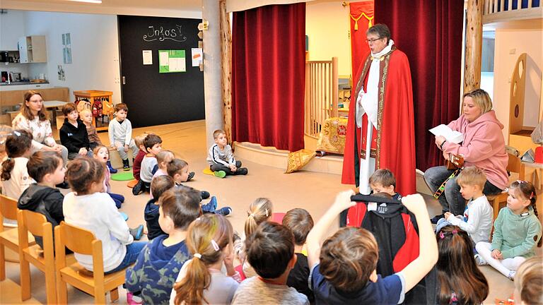 Aufmerksam hören die Kinder zu, als ihnen Pfarrer Amrehn die Lebensgeschichte des Patrons 'ihres' Kindergartens, des Heiligen Sebastian erzählt. Rechts im Bild Miriam Hetzel aus dem Team des Kindergartens, die die Lieder der Kinder mit ihrer Gitarre begleitet.