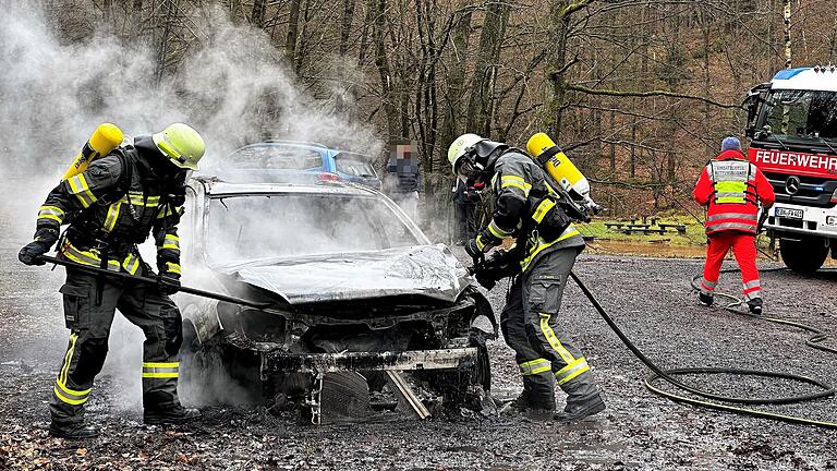 Einsatzkräfte der Feuerwehr Ebern löschen das brennende Auto unter schwerem Atemschutz.