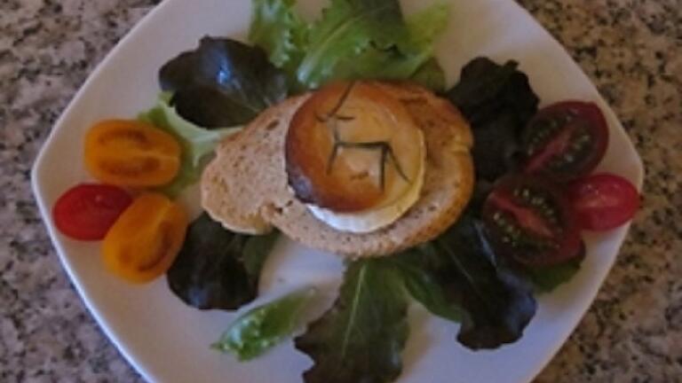 Der gratinierte Ziegenkäse mit Baguette wird auf Salat angerichtet.