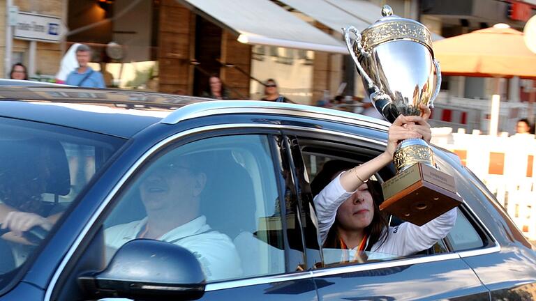 Gut festhalten: Mit dem Pokal fuhr die siegreiche Mannschaft auf den Marktplatz in Bad Königshofen, Dina Belenkaja präsentiert ihn, Jürgen Müller sitzt am Steuer.